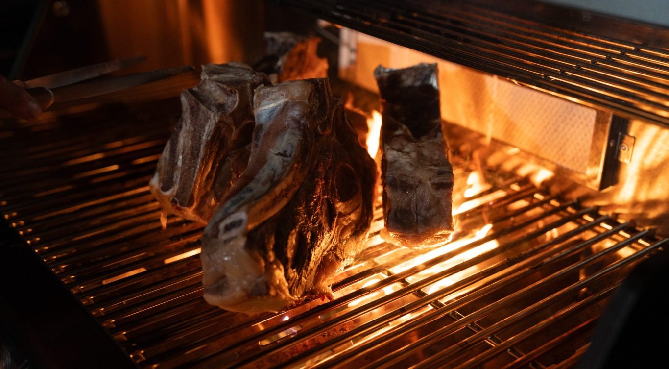 Ein Stück Fleisch liegt auf einem Grill und ist vom Feuer umgeben.